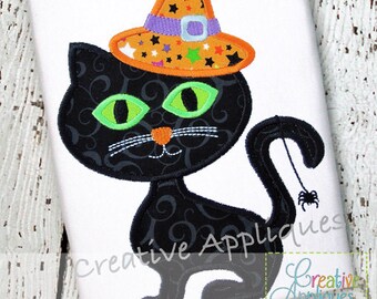 Puede incluir: Gato negro con ojos verdes que lleva un sombrero de bruja con detalles en naranja, morado y verde. El sombrero tiene una hebilla negra y estrellas blancas. La cola del gato tiene una araña en el extremo. La imagen tiene el texto "Creative Appliques" en la parte inferior.