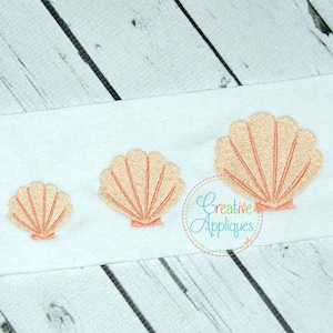 Op de afbeelding: Drie geborduurde schelpen in verschillende maten, in licht roze kleur, op een witte stoffen achtergrond.