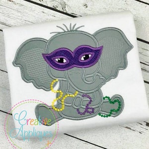 May include: Embroidered design of a gray elephant wearing a purple mask and a string of green and yellow beads. The elephant is sitting down with its legs crossed.