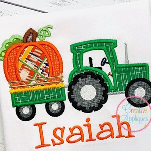 May include: Embroidered design of a green tractor pulling a wagon with a pumpkin inside. The name Isaiah is embroidered below the tractor.