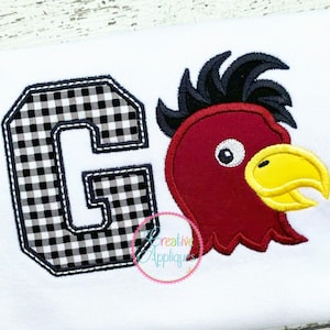 Pode incluir: Design bordado com uma letra G xadrez preto e branco e um galo vermelho com bico amarelo. O design está sobre um fundo de tecido branco.