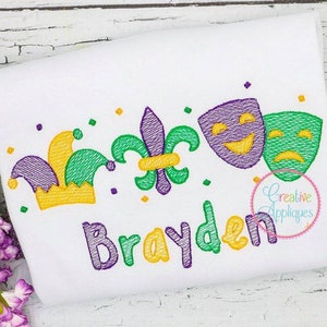 May include: A white t-shirt with a purple, green, and yellow embroidered design featuring a jester's hat, a fleur-de-lis, and two masks. The name "Brayden" is embroidered in purple and yellow below the design.