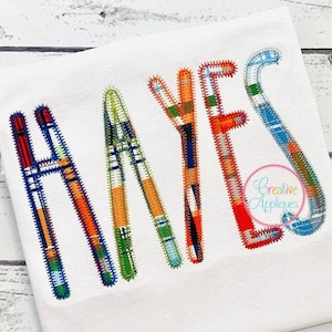 May include: A white t-shirt with the name "HAYES" embroidered in colorful patchwork fabric letters.