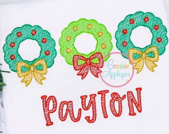 Op de afbeelding: Drie groene kerstkransen met rode en gouden strikken, met de naam Payton eronder geborduurd in rood.