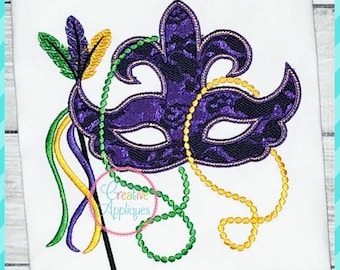 May include: Embroidered purple Mardi Gras mask with a fleur-de-lis design, green and gold beaded necklaces, and colorful feathers. The mask is on a white background with the text "Creative Appliques".