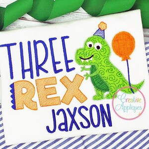 Op de afbeelding: Borduurwerk op een witte stof met een groene dinosaurus die een feestmuts draagt, een ballon vasthoudt en de tekst "THREE REX Jaxson".