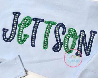 May include: A light blue long-sleeved shirt with the name "Jettson" embroidered in green and blue plaid.