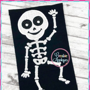 May include: White skeleton with a smiling face and raised arm, embroidered on a black fabric. The skeleton is in a standing position with its legs slightly bent.