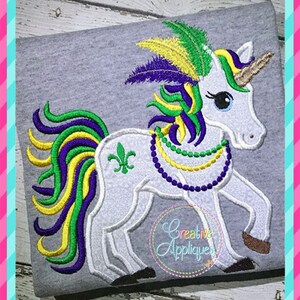 May include: White unicorn with a purple, green, and yellow mane and tail. The unicorn is wearing a purple, green, and gold beaded necklace and a purple, green, and yellow feathered headdress. The unicorn is standing on a gray background.