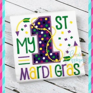 Könnte beinhalten: Ein weißes T-Shirt mit einem gestickten Design in Lila, Grün und Gelb, das "My 1st Mardi Gras" sagt.