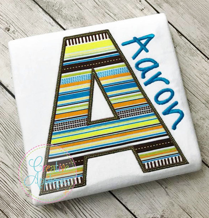 May include: A white t-shirt with a large, colourful striped letter A and the name "Aaron" embroidered in blue thread.