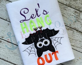 Puede incluir: Camiseta blanca con un diseño bordado de un murciélago colgado boca abajo con el texto "Let's Hang Out" en verde, morado y naranja.