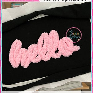 May include: A pink yarn "hello" appliqu&eacute; on a black fabric background. The appliqu&eacute; is available in 7 sizes: 2 inches, 2.5 inches, 3 inches, 4 inches, 5 inches, 6 inches, and 7 inches.