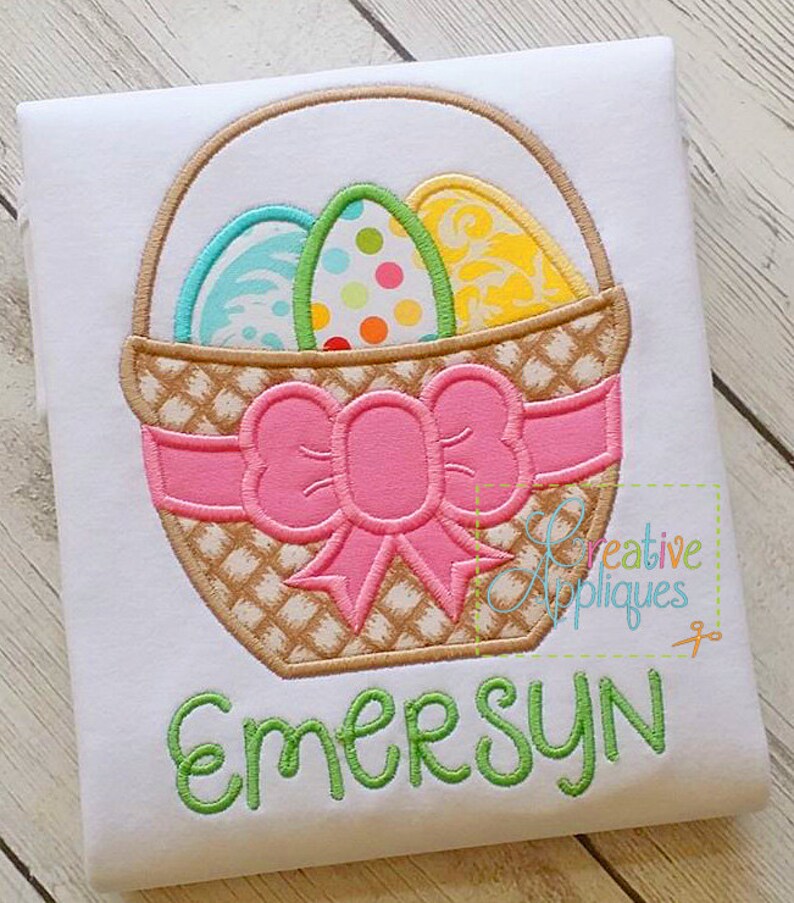 May include: Embroidered design of a brown wicker basket with a pink bow and three colourful Easter eggs. The name "Emersyn" is embroidered below the basket.