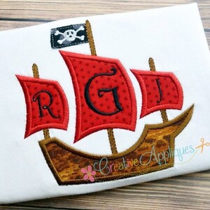 Könnte beinhalten: Gestickte Darstellung eines roten und braunen Piratenschiffs mit drei Segeln. Die Segel sind mit den Buchstaben R, G und J bestickt. Das Schiff hat eine schwarze Piratenflagge mit einem Totenkopf und Knochen.