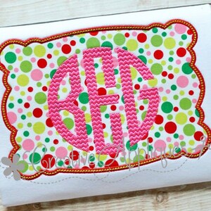 May include: A pink monogram letter in a circle on a white background with a red, green, and pink polka dot pattern inside a scalloped frame with a gold outline.