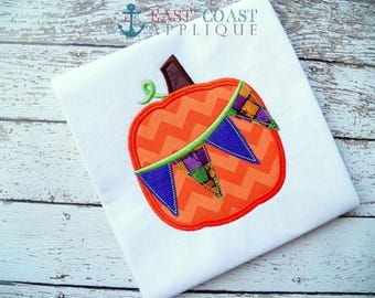 May include: Orange pumpkin with a chevron pattern and a green and purple banner with triangular flags. The pumpkin is embroidered on a white t-shirt.