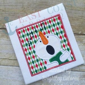 May include: A white snowman with a green scarf and orange nose sings in a red and green checkered frame. The text "Stitched by Brightley Colored Sparkles Creations" is below the frame.