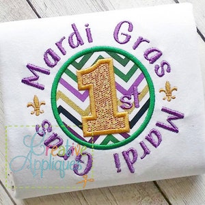 Könnte beinhalten: Lila und grünes Stickmuster mit einer goldenen Nummer eins und dem Text "Mardi Gras 1. Mardi Gras" auf einem weißen T-Shirt.