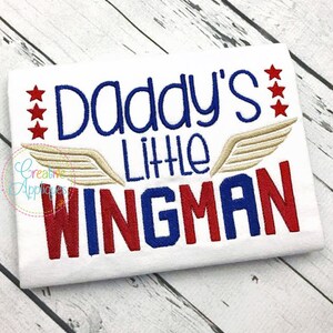 May include: White t-shirt with red, white, and blue embroidery that reads "Daddy's Little Wingman" with gold wings.