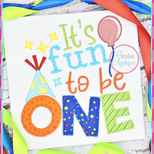 May include: It's fun to be one embroidery design with a party hat, balloon, and stars. The letters are colorful and patterned.