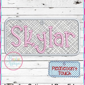 Op de afbeelding: Een roze geborduurd naamschild met de naam "Skylar" op een grijze achtergrond. Het schild heeft een zilveren rand en een klein gaatje bovenaan. Een kleiner schild eronder zegt "Aangeraakt mag niet worden".