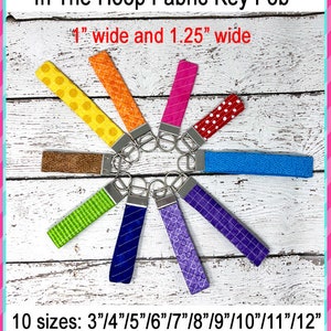 May include: Ten fabric key fobs in various colors and patterns, arranged in a circle on a white wooden background. The key fobs are 1 inch wide and 1.25 inches wide. The text "In The Hoop Fabric Key Fob" is at the top of the image. The text "10 sizes: 3"/4"/5"/6"/7"/8"/9"/10"/11"/12" is at the bottom of the image. The text "5 stitch types: diamond, diagonal, lines, square, stipple" is below the sizes.