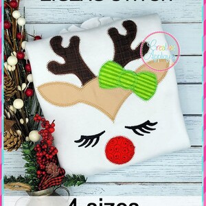 Puede incluir: Diseño de bordado de cara de reno en punto de zigzag en 4 tamaños. El diseño presenta un reno marrón con un lazo verde, ojos cerrados con pestañas y una nariz roja.