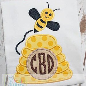 May include: A yellow and black bee with a smiling face flies over a yellow and brown beehive with a brown circle monogram that says "CBD".