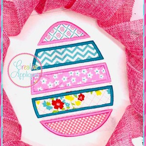 Op de afbeelding: Een geborduurd paasei-ontwerp in roze en blauw met verschillende patronen, waaronder stippen, bloemen en chevron-strepen.