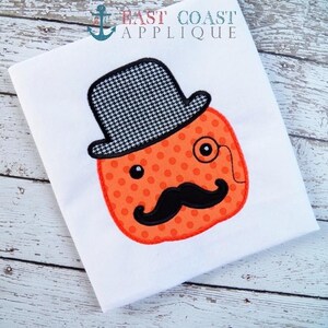May include: Orange pumpkin with a black and white patterned top hat, a black mustache, and a small red monocle. The pumpkin is on a white background.