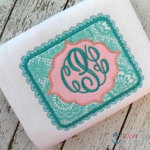 May include: An embroidered design in teal and pink featuring a monogram in a square frame with a lace pattern.
