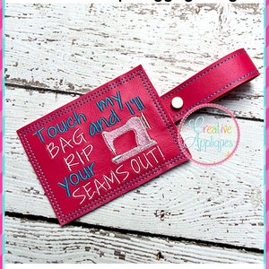May include: Pink leather luggage tag with blue embroidery that reads "Touch my bag and I'll rip your seams out!" with a pink sewing machine graphic. The tag is 5x7 inches and has a loop for attaching to luggage.
