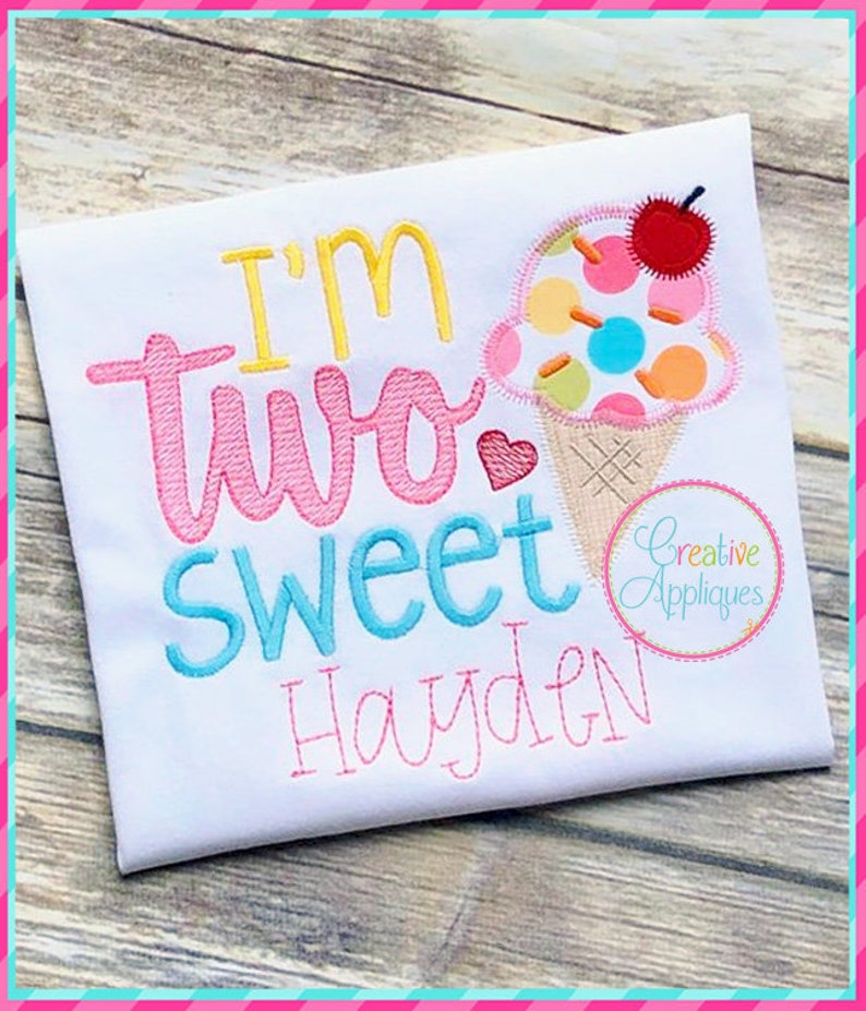 May include: A white onesie with the text "I'm two sweet Hayden" embroidered in pink, blue, and yellow. A pink heart and an ice cream cone with a cherry on top are also embroidered on the onesie.
