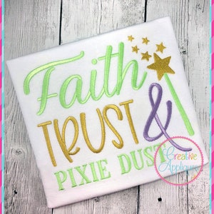 May include: White t-shirt with embroidered text reading "Faith, Trust & Pixie Dust." The words are in green, gold, and purple, with a gold star and wand design. The shirt is on a light wood background.