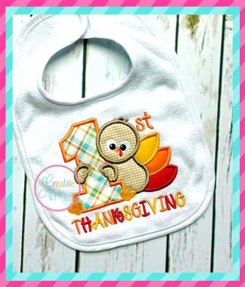 May include: White baby bib with an embroidered design of a turkey with a plaid number one and the text "1st Thanksgiving".