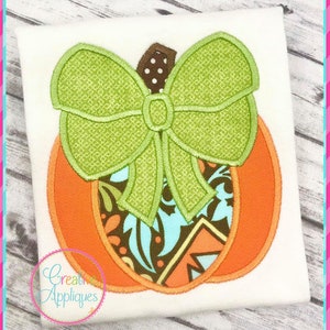 May include: An orange pumpkin with a green bow on top. The pumpkin has a patterned design inside.