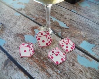 May include: Four white fabric dice with pink dots, used as wine glass charms. The dice are hanging from a wine glass.