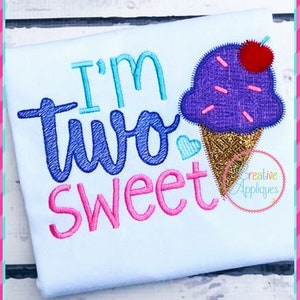 May include: Embroidered design on a white t-shirt featuring an ice cream cone with sprinkles and a cherry on top. The text "I'm two sweet" is embroidered in blue, pink, and turquoise.