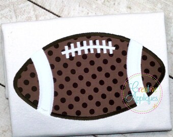 May include: A brown and white football with a polka dot pattern. The football is embroidered on a white t-shirt.