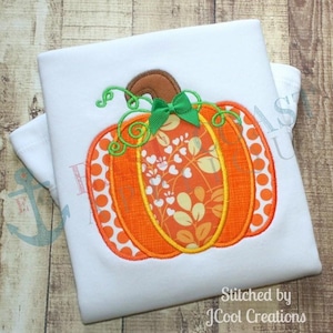 May include: White t-shirt featuring an embroidered orange pumpkin with a green bow and stem. The pumpkin has a patterned center and polka dot edges. The text "Stitched by JCool Creations" is at the bottom.