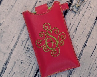 May include: A bright pink phone case with a green embroidered monogram. The case has a yellow stitch around the edges and a silver key chain attached.