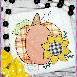 Puede incluir: Diseño de aplique bordado con una calabaza con estampado de cuadros y un girasol con un centro a cuadros blanco y negro. El diseño es perfecto para manualidades y proyectos de otoño.
