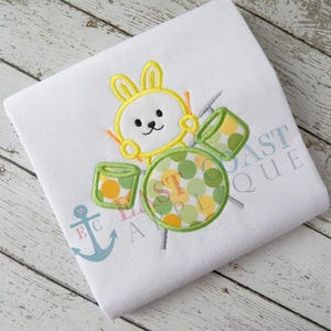 May include: A yellow bunny rabbit with green and yellow polka dot drums. The bunny is playing the drums with two drumsticks.