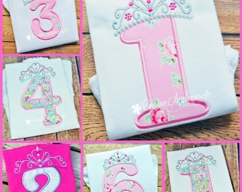 May include: Six embroidered designs of numbers 1, 2, 3, 4, 6, and 1 with a silver crown on top. The numbers are pink and white with floral patterns. The designs are on white and pink t-shirts.