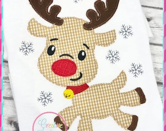 May include: White fabric featuring a reindeer applique with a red nose, brown antlers, and a gold bell. The reindeer is made of tan and white checkered fabric. Embroidered snowflakes surround the reindeer. The text "Creative Appliques" is in a pink circle.