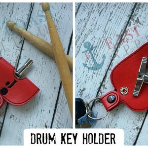May include: Red leather drum key holder with a silver drum key. The holder is attached to a key ring and has a small black and white drum symbol on the front.