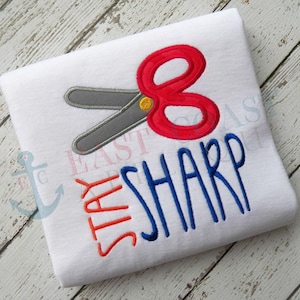 May include: White t-shirt with a red and gray pair of scissors and the text "Stay Sharp" in blue and orange.