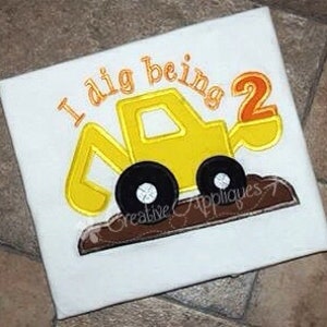 May include: Yellow embroidered applique of a construction vehicle with the text "I dig being 2" on a white t-shirt.