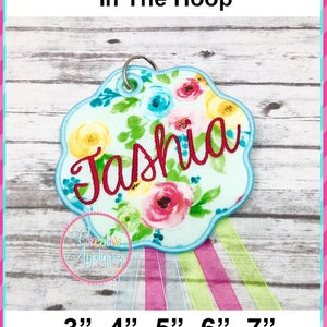 May include: A light blue, floral embroidery design with the name "Tashia" in red lettering. The design is available in 3", 4", 5", 6", and 7" sizes.